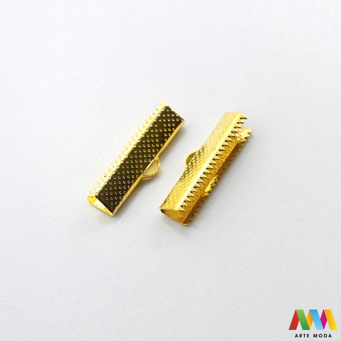 Metalni stiskači i završeci sa zubima za izradu nakita u srebrnoj, zlatnoj i brončanoj boji složeni na radnoj površini. Prikazani su ravni stiskači za tekstilne trake, baršun, antilop i plosnate kožice s integriranom omčicom za spajanje s kopčama i produžnim lančićima. Kvalitetan repromaterijal za uredno fiksiranje krajeva pri izradi choker ogrlica, narukvica i modnih dodataka u DIY radionicama za ručnu izradu unikatnog nakita s nazubljenim rubovima koji jamče čvrst prihvat bez ispadanja materijala.