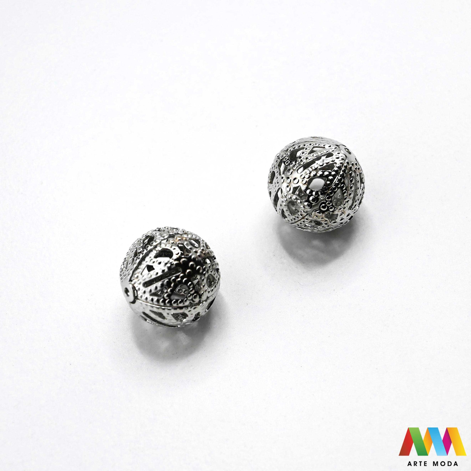 Elegantne metalne filigranske perle u srebrnoj, zlatnoj i nikal boji izložene na površini za izradu nakita. Prikazane su šupljikave i čipkaste metalne kuglice te ovalni filigranski distanceri s raznolikim vintage i orijentalnim uzorcima. Kvalitetan metalni repromaterijal i lagani razdjelnici s izbušenim rupama za provlačenje konca i igala, namijenjeni za izradu unikatnih narukvica, visećih naušnica i bogatih ogrlica u kreativnim DIY radionicama za izradu ručno rađenog modnog nakita arte moda repromaterijali