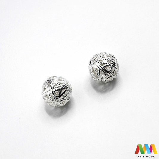 Elegantne metalne filigranske perle u srebrnoj, zlatnoj i nikal boji izložene na površini za izradu nakita. Prikazane su šupljikave i čipkaste metalne kuglice te ovalni filigranski distanceri s raznolikim vintage i orijentalnim uzorcima. Kvalitetan metalni repromaterijal i lagani razdjelnici s izbušenim rupama za provlačenje konca i igala, namijenjeni za izradu unikatnih narukvica, visećih naušnica i bogatih ogrlica u kreativnim DIY radionicama za izradu ručno rađenog modnog nakita arte moda repromaterijali